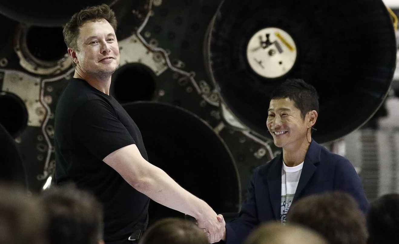 Илон Маск жмет руку ямонскому космическому туристу на фоне ракетоносителя.