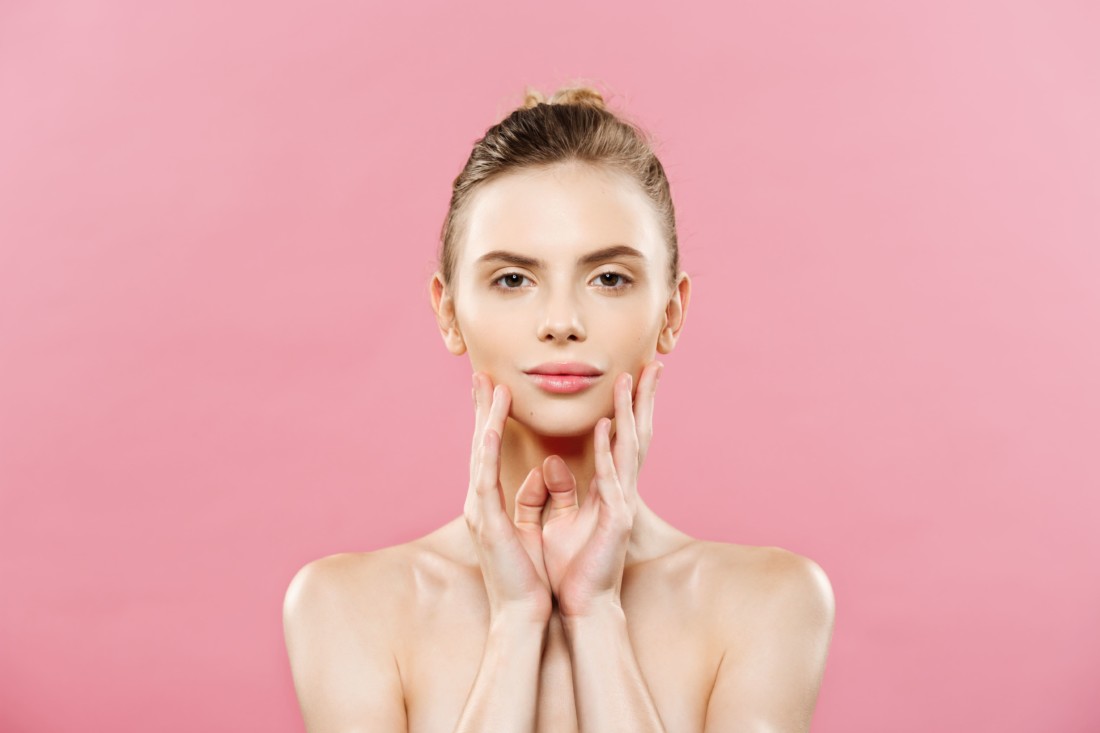 концепция красоты и здоровой кожи: девушка с чистой сияющей кожей на розовом фоне