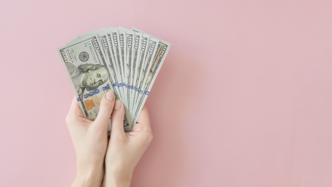купюры доллара в руках на розовом фоне
