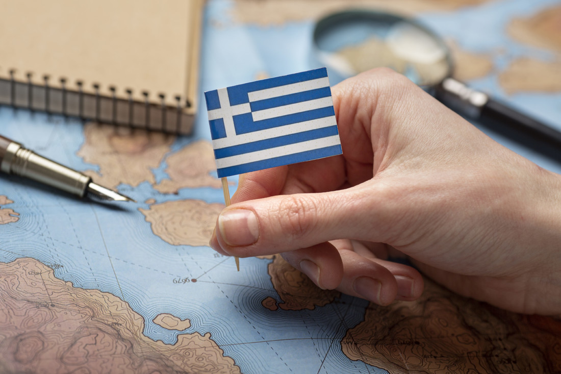 маленький флаг греции в женской руке на фоне лежащей карты