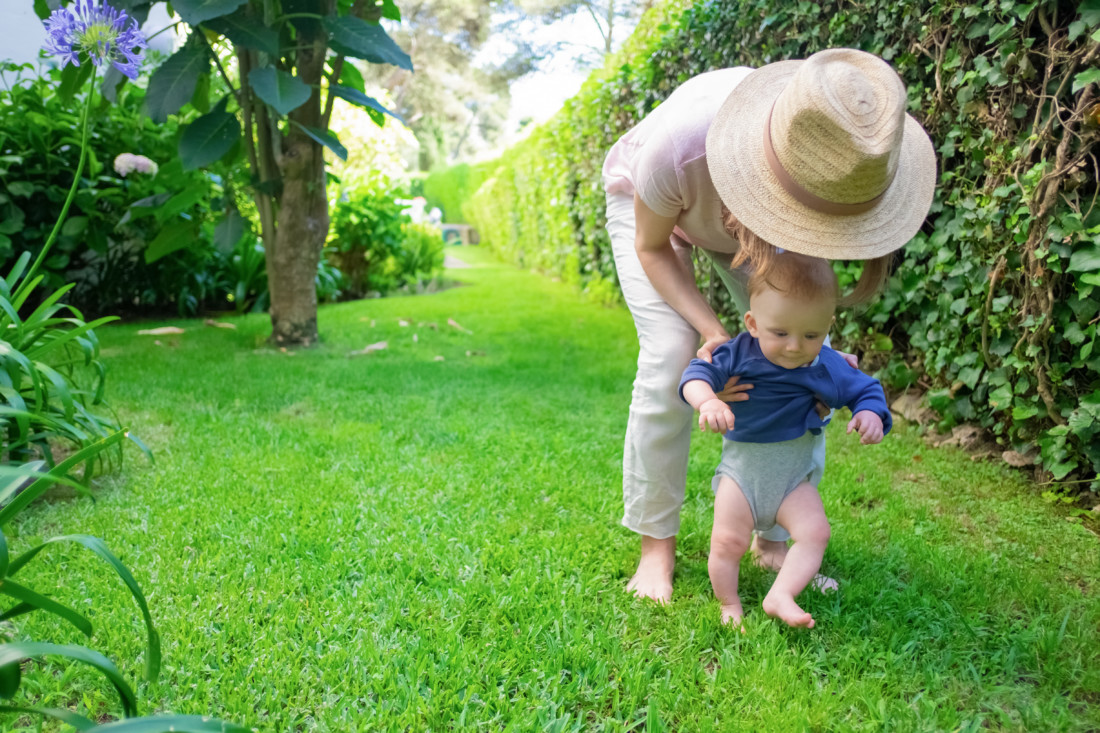мама ведет маленького ребенка босиком по зеленой траве