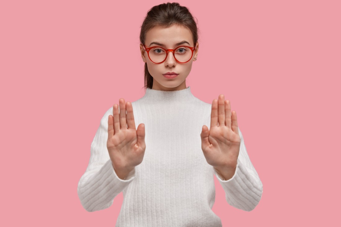 девушка в очках на розовом фоне показывает жест стоп потому что не хочет спорить