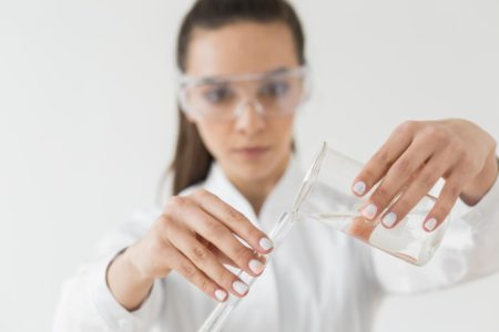 женщина ученый в защитных очках переливает из одной емкости в другую на светлом фоне вид спереди