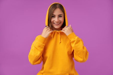 улыбающаяся девушка в желтом худи на фиолетовом фоне